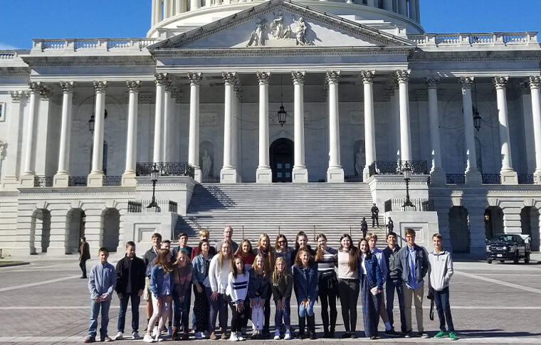 students outside the Capitol building columns and engraved stone carvings